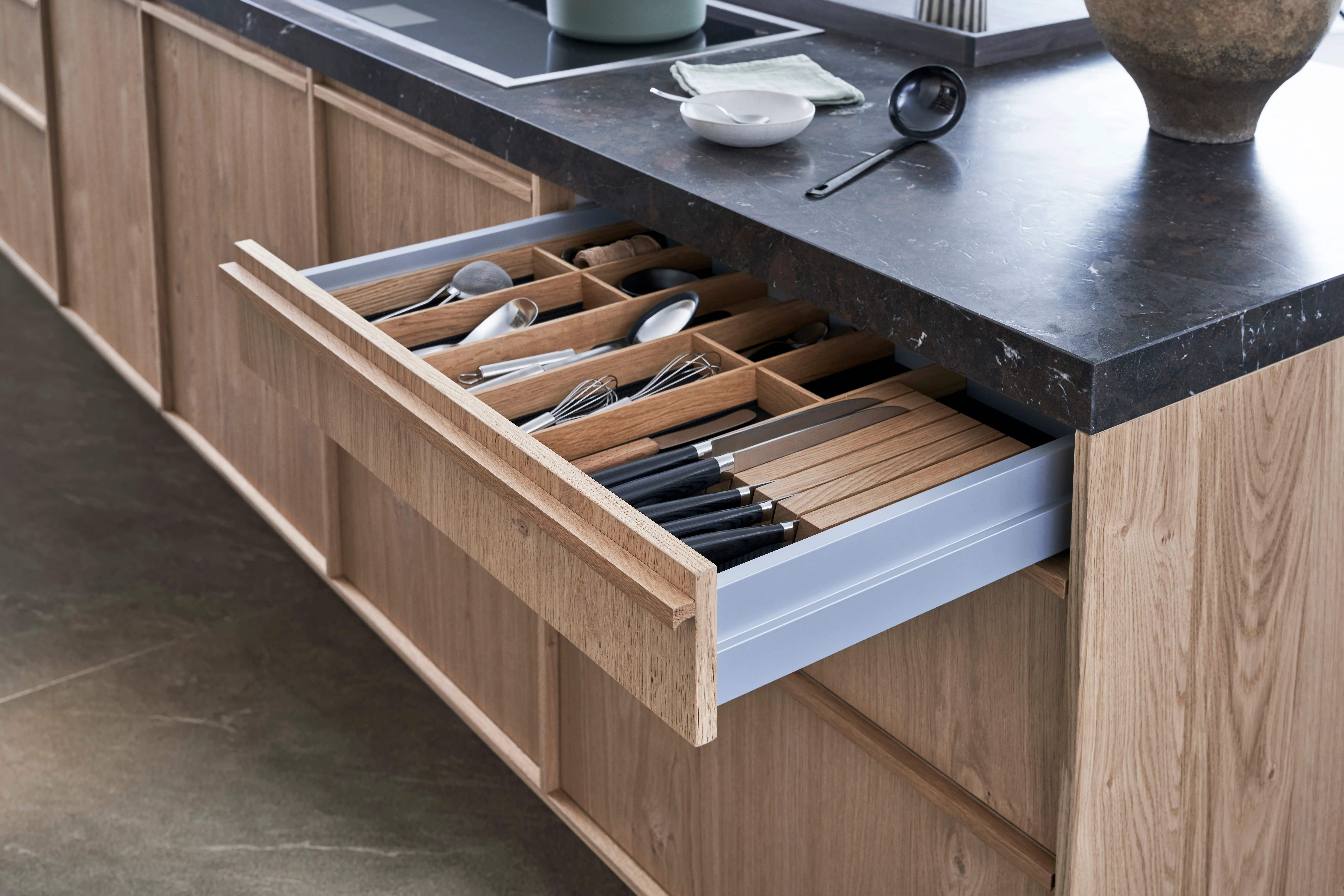 Geöffnete Schublade mit Holz-Besteckeinsatz unter dunkler Steinarbeitsplatte