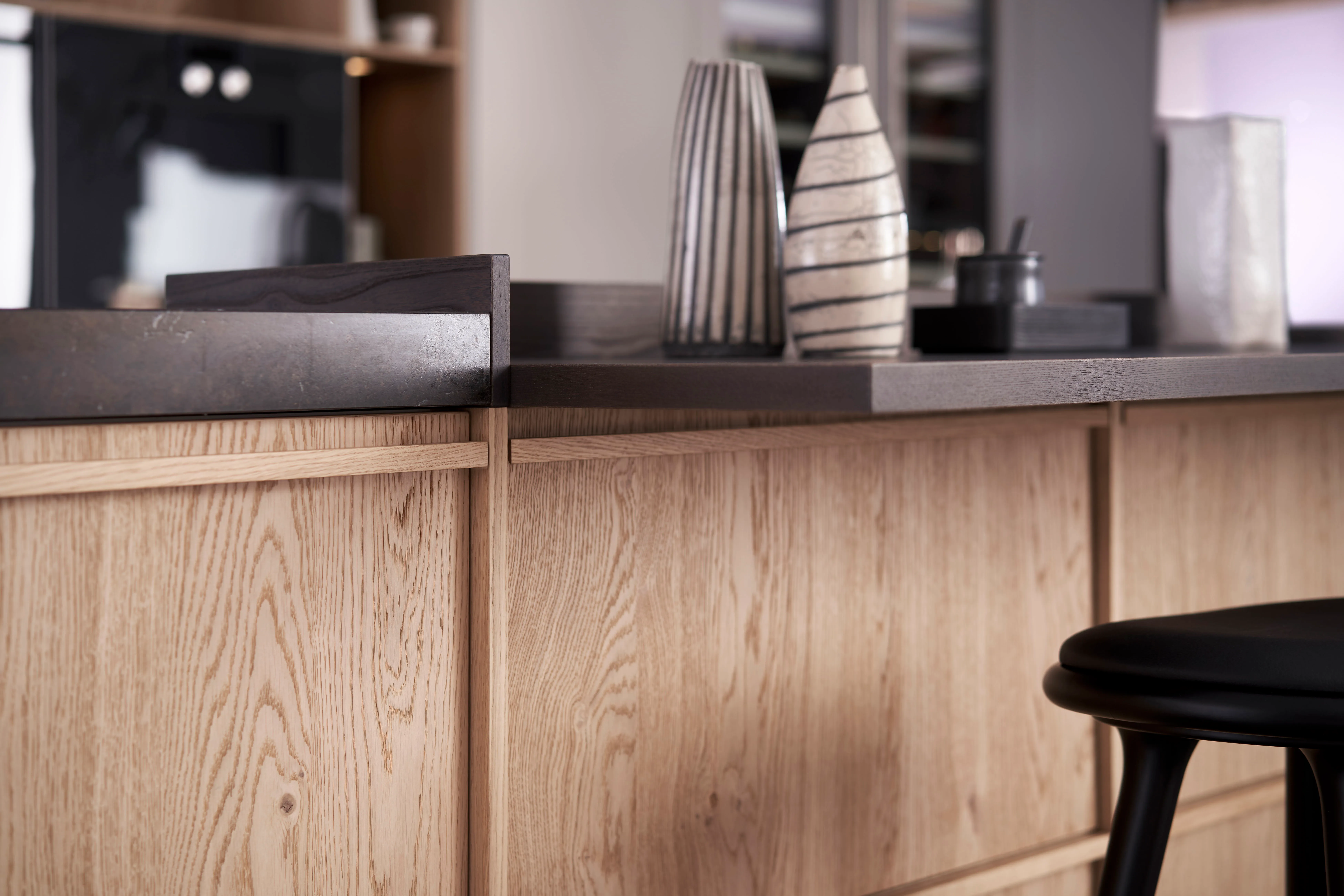 Nahaufnahme der Kücheninsel – Eichenholzfront mit dunkler Steinarbeitsplatte und dekorativen Vasen