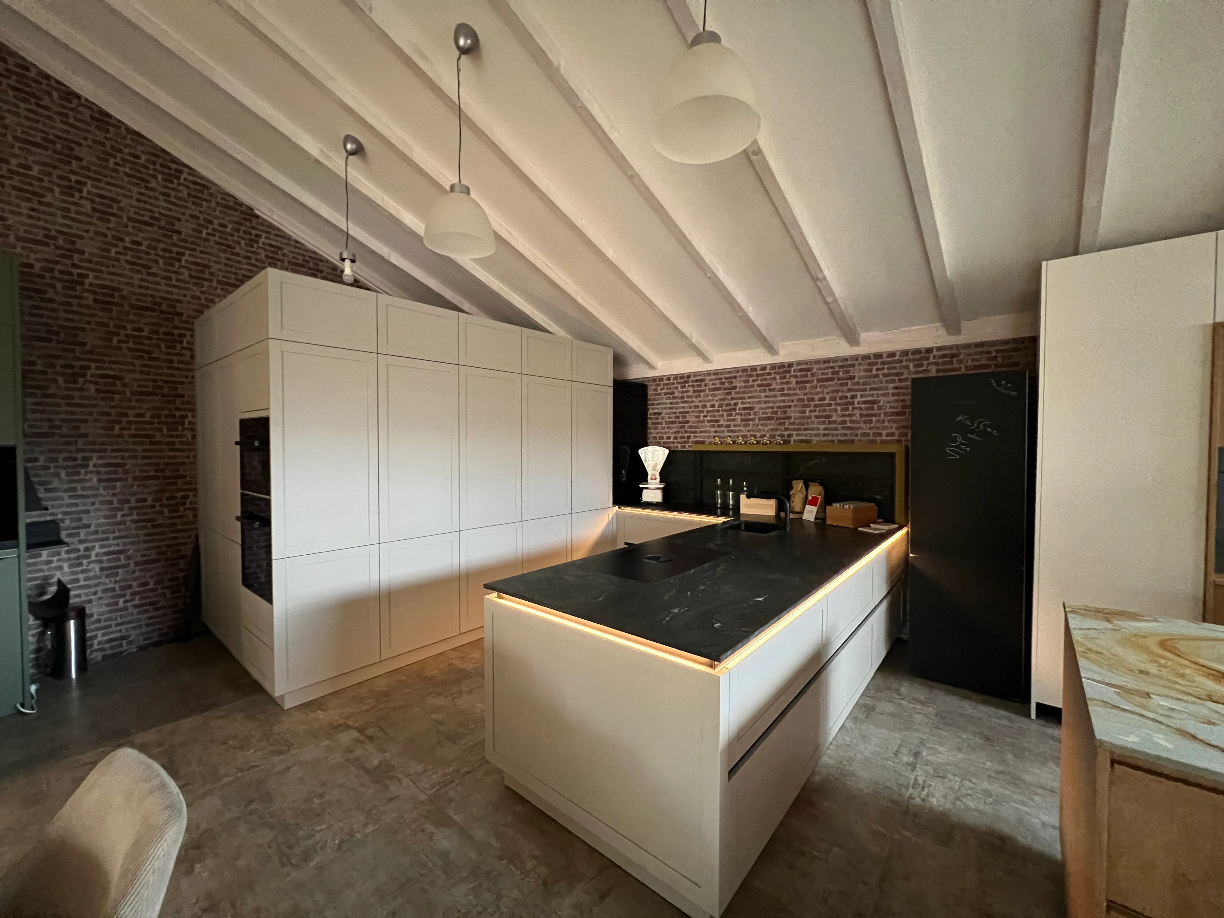 Weitwinkelansicht der Küchenausstellung mit weißer Küche und beleuchtetem Kochblock