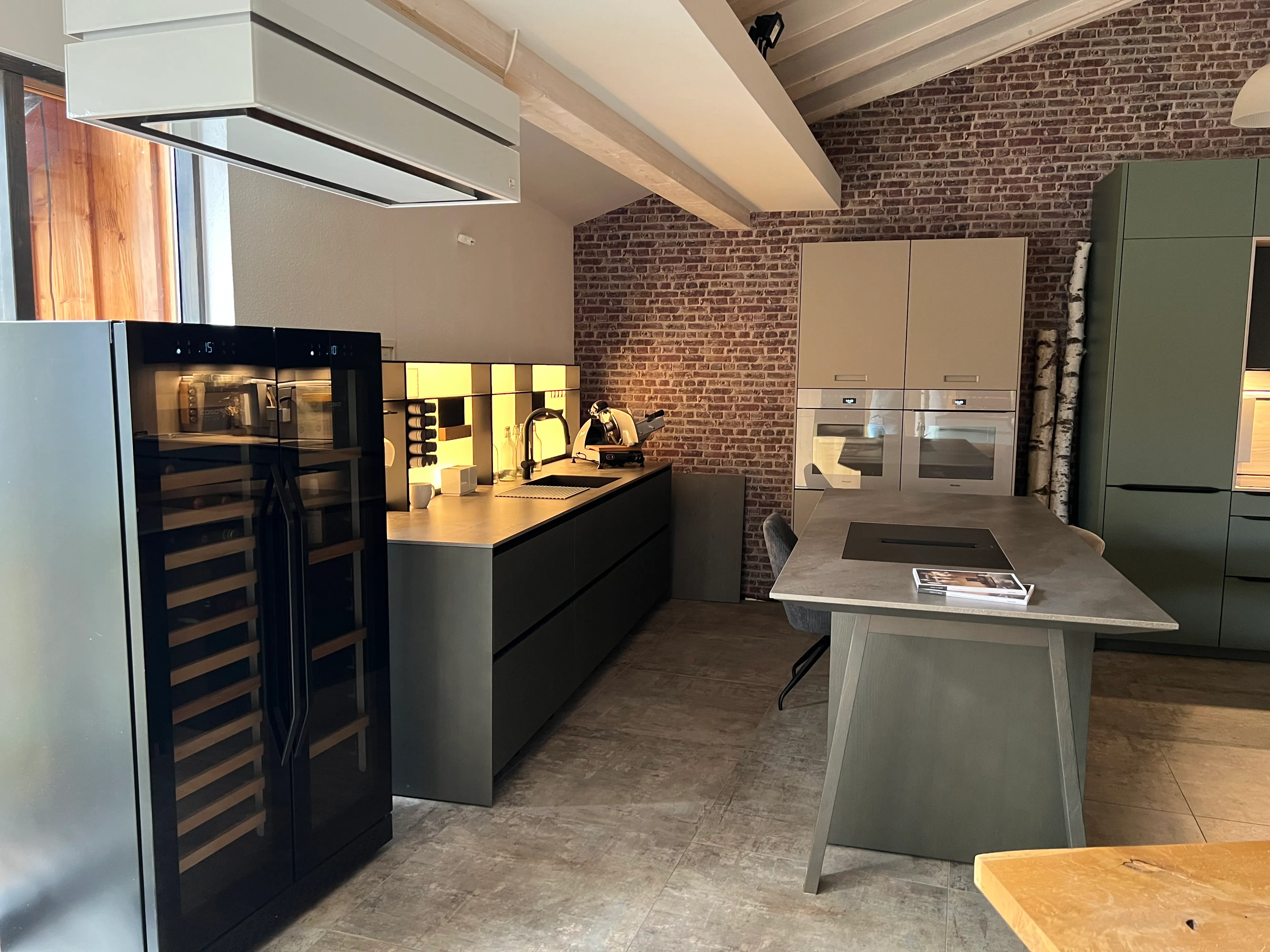 Gesamtansicht der Küchenausstellung mit grauer Kücheninsel und grüner Wandküche